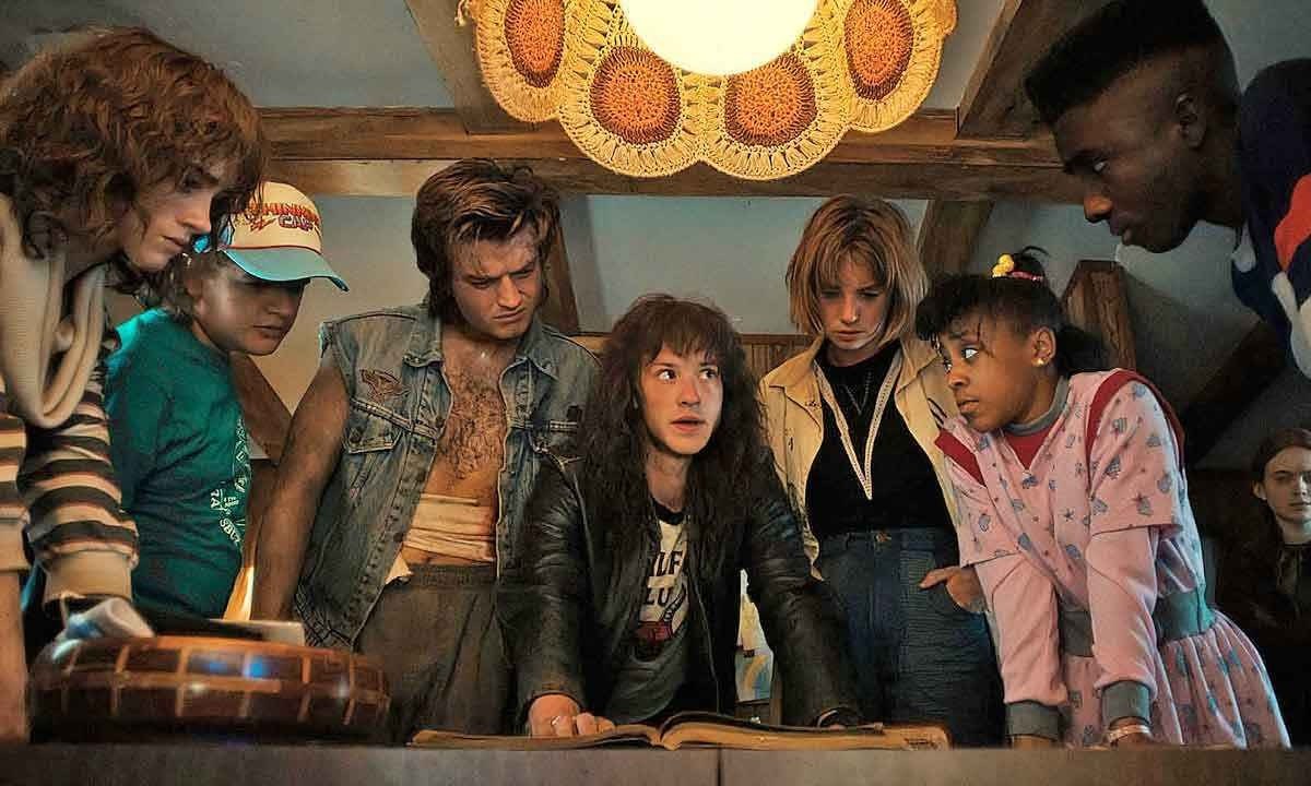 Reunidos em torno de uma mesa, com um lustre aceso sobre suas cabeças, atores de stranger things se entreolham -  (crédito: NETFLIX/DIVULGAÇÃO)