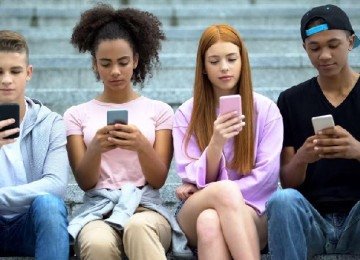 Adolescentes brancos e negros sentados em uma escada olhando para seus celulares -  (crédito: Getty Images)