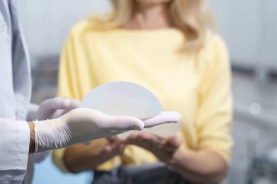 Médico segurando prótese de silicone, ao fundo paciente sentada na maca -  (crédito: Freepik)