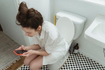 Mulher usando celular sentada no vaso sanitário -  (crédito: Pexels)