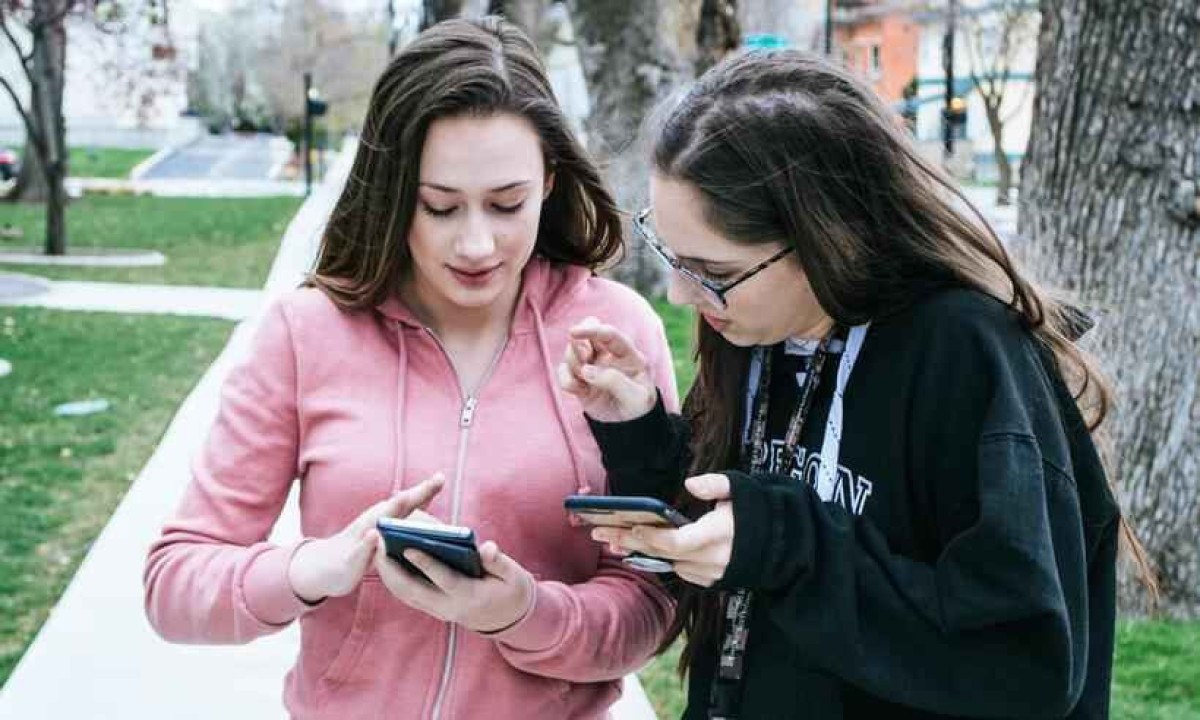 Duas meninas brancas estão olhando para seus celulares enquanto andam - (crédito: Pexels/Brett Sayles)