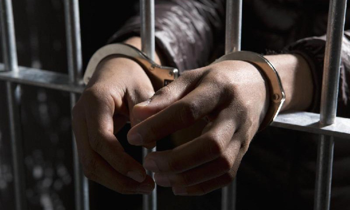 Mãos de pessoa algemada atrás das grades -  (crédito: Getty Images)