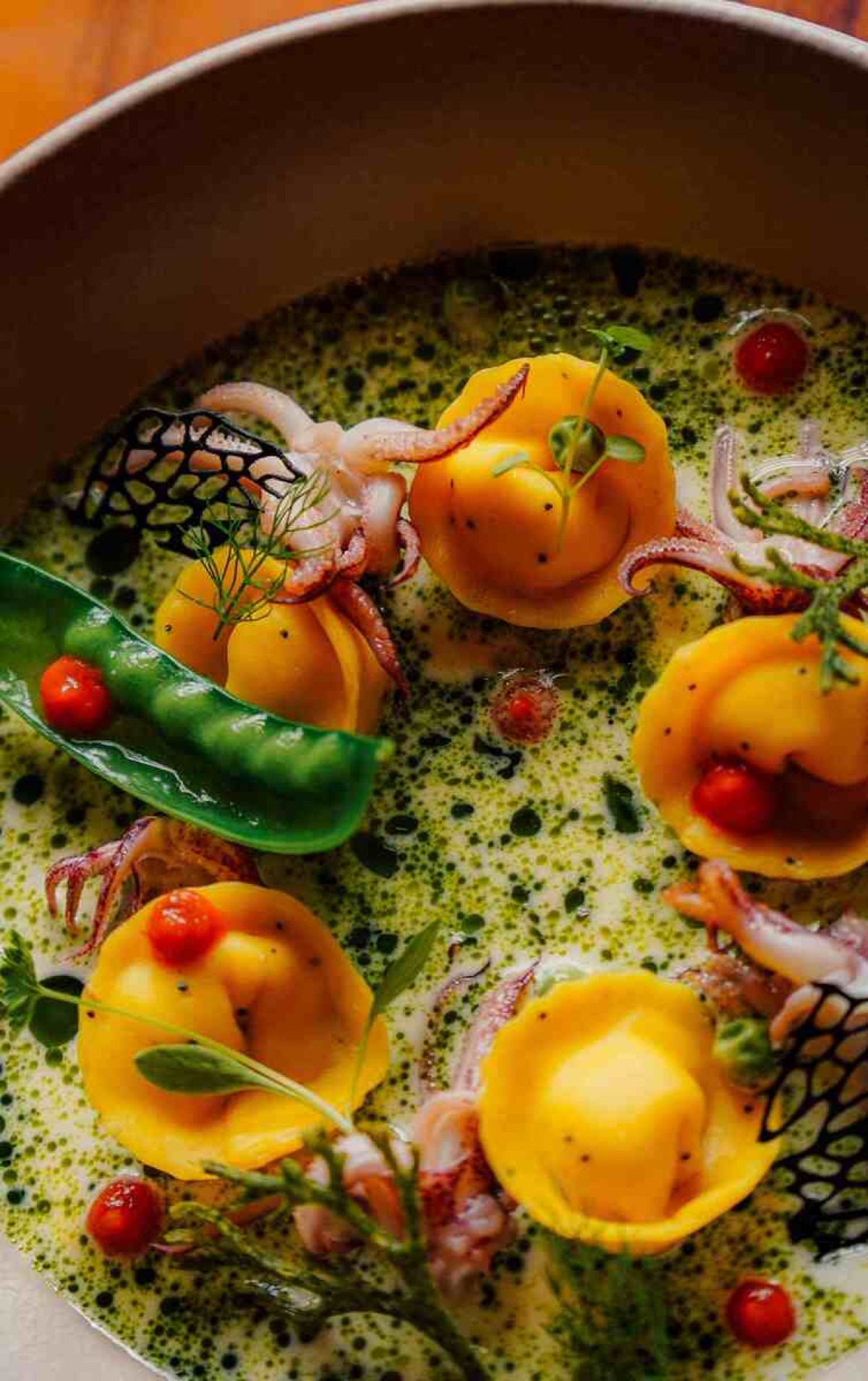Ravióli de camarão com cabecinhas de lula flambadas na cachaça, ervilhas tortas, ervas frescas, creme de espumante e óleo de manjericão