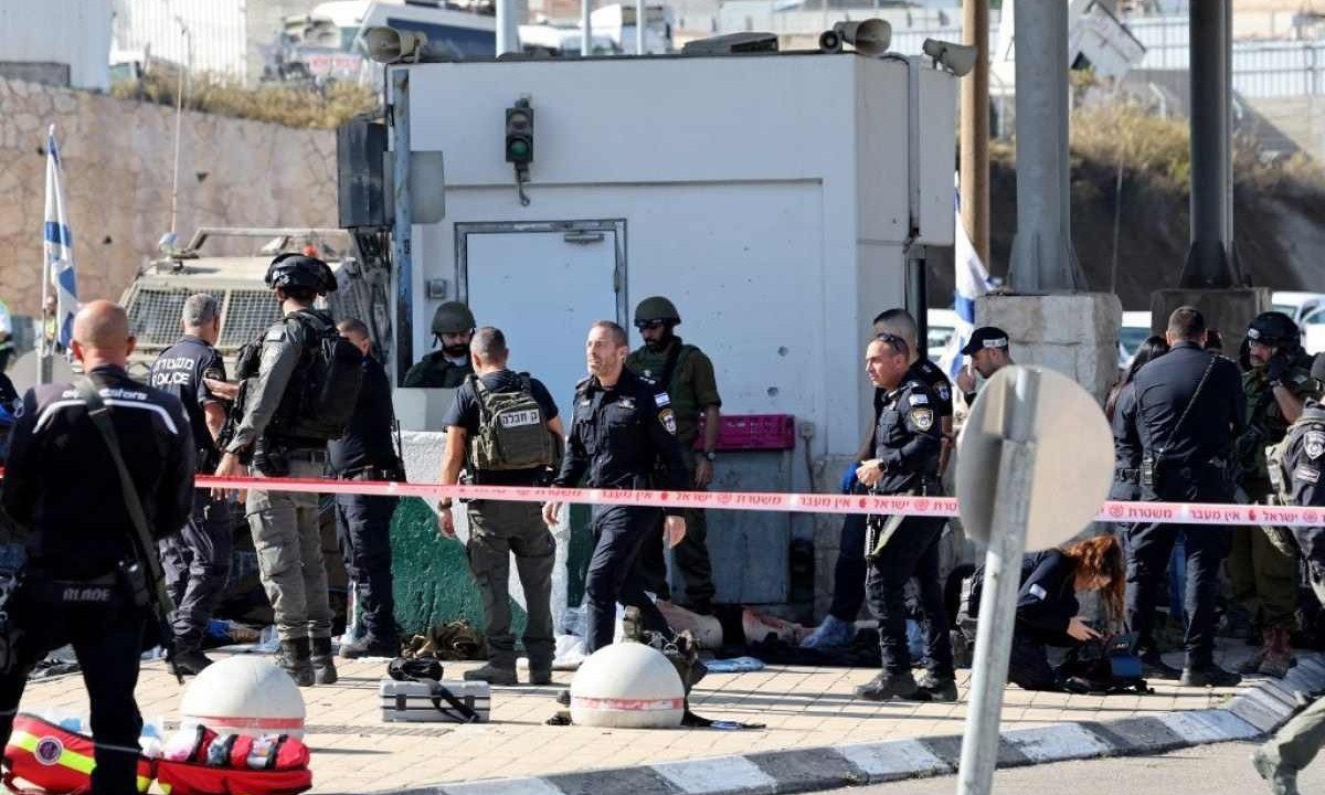 
Policiais israelenses cercam corpo no chão, próximo ao posto de controle atacado
       -  (crédito:  AHMAD GHARABLI / AFP)