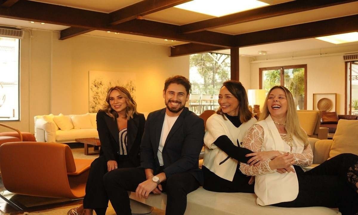 Quatro pessoas brancas, um homem e tr&ecirc;s mulheres, sentadas em um banco sorriem para foto.       