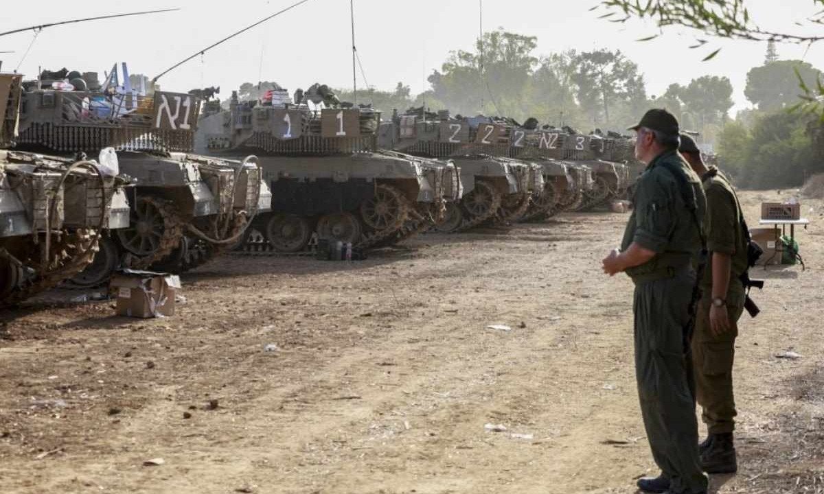 Soldados conversam em frente a um grupo de tanques parados na fronteira de Israel com Gaza -  (crédito: Menahem KAHANA / AFP)
