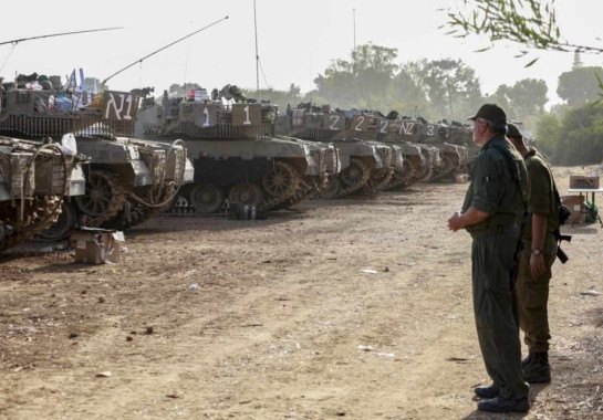 Soldados conversam em frente a um grupo de tanques parados na fronteira de Israel com Gaza -  (crédito: Menahem KAHANA / AFP)