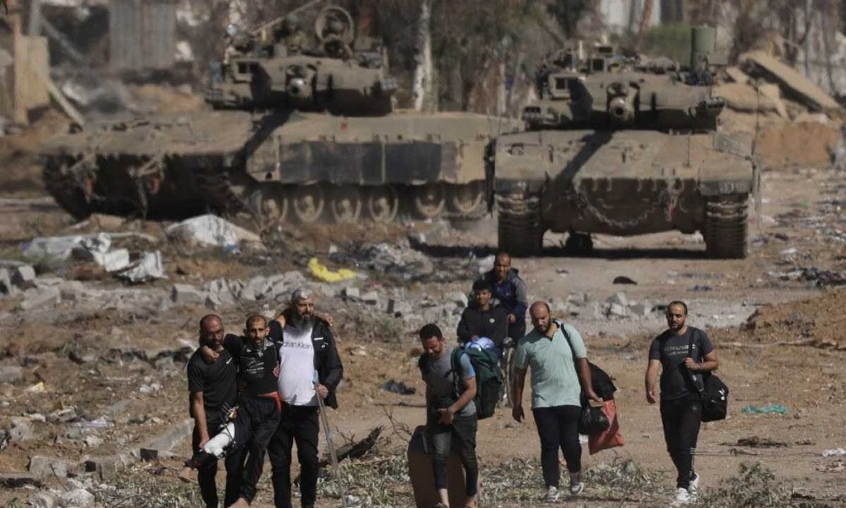 Palestinos que fogem do norte pela estrada Salaheddine ajudam um homem com uma perna enfaixada enquanto caminham em frente aos tanques do exército israelense no distrito de Zeitoun, na periferia sul da Cidade de Gaza -  (crédito: Mahmud Hams / AFP)