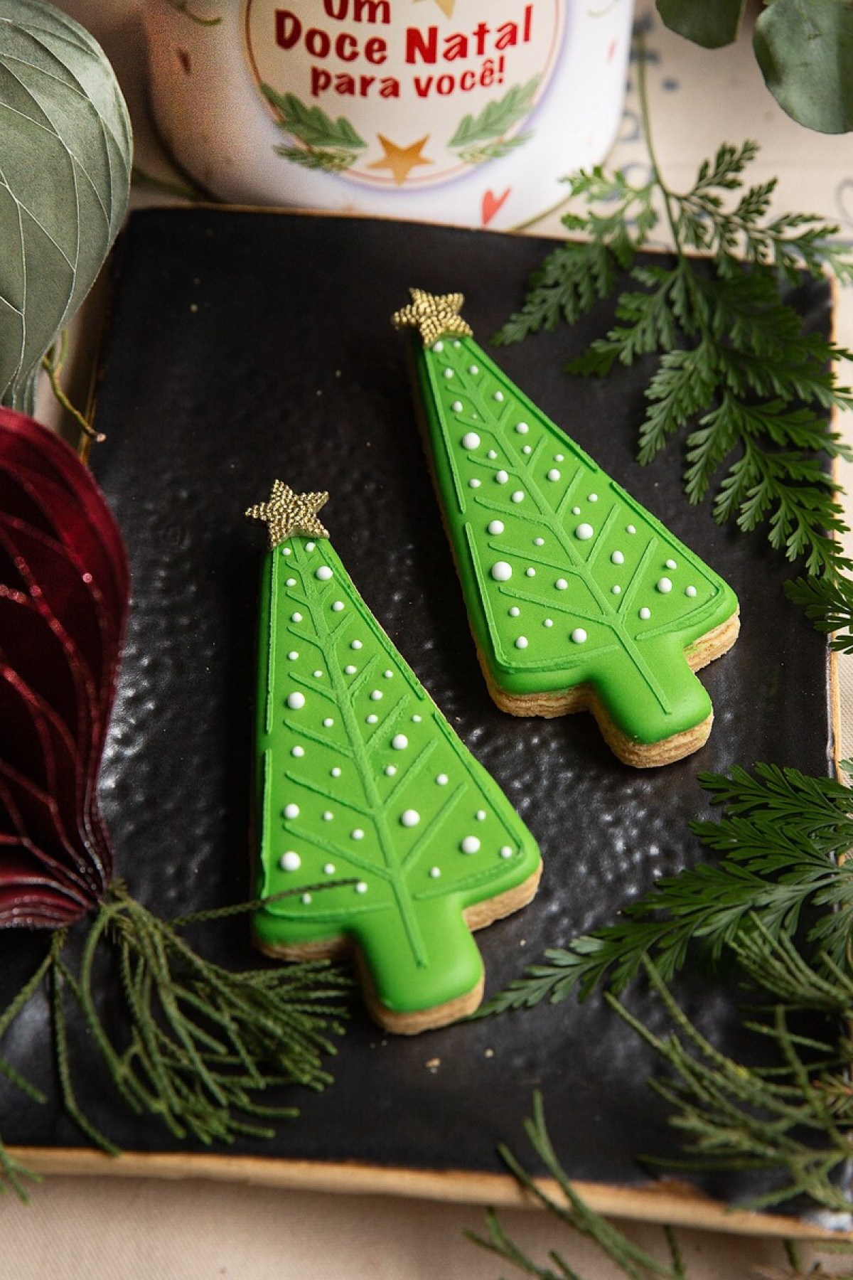 O biscoito decorado mais vendido da Sweet Ana tem formato de árvore, glacê verde, bolinhas brancas simulando neve e estrela dourada 