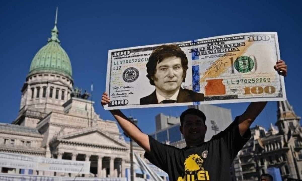 Um apoiador do presidente eleito da Argentina, Javier Milei, exibe um cartaz com uma nota de cem dólares com a imagem do futuro presidente enquanto espera do lado de fora do Congresso antes de sua cerimônia de posse, em Buenos Aires, em 10 de dezembro de 2023. -  (crédito: Luis ROBAYO / AFP)