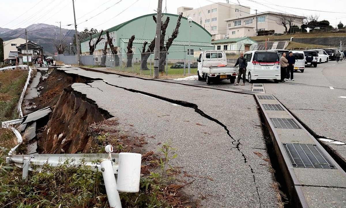 Pessoas próximas a grandes rachaduras na calçada após evacuarem para uma rua na cidade de Wajima, no Japão -  (crédito: Yusuke FUKUHARA / Yomiuri Shimbun / AFP)