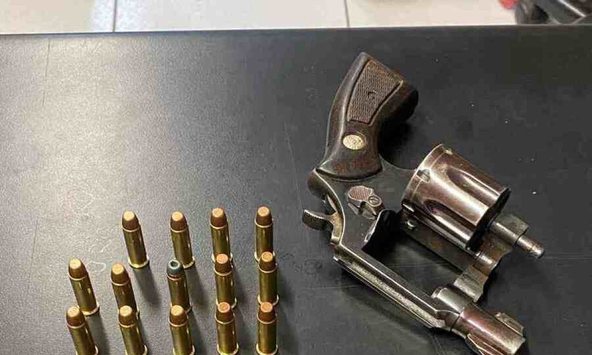 Na foto aparece uma arma de fogo e munições dispostas em cima de uma mesa de metal. 