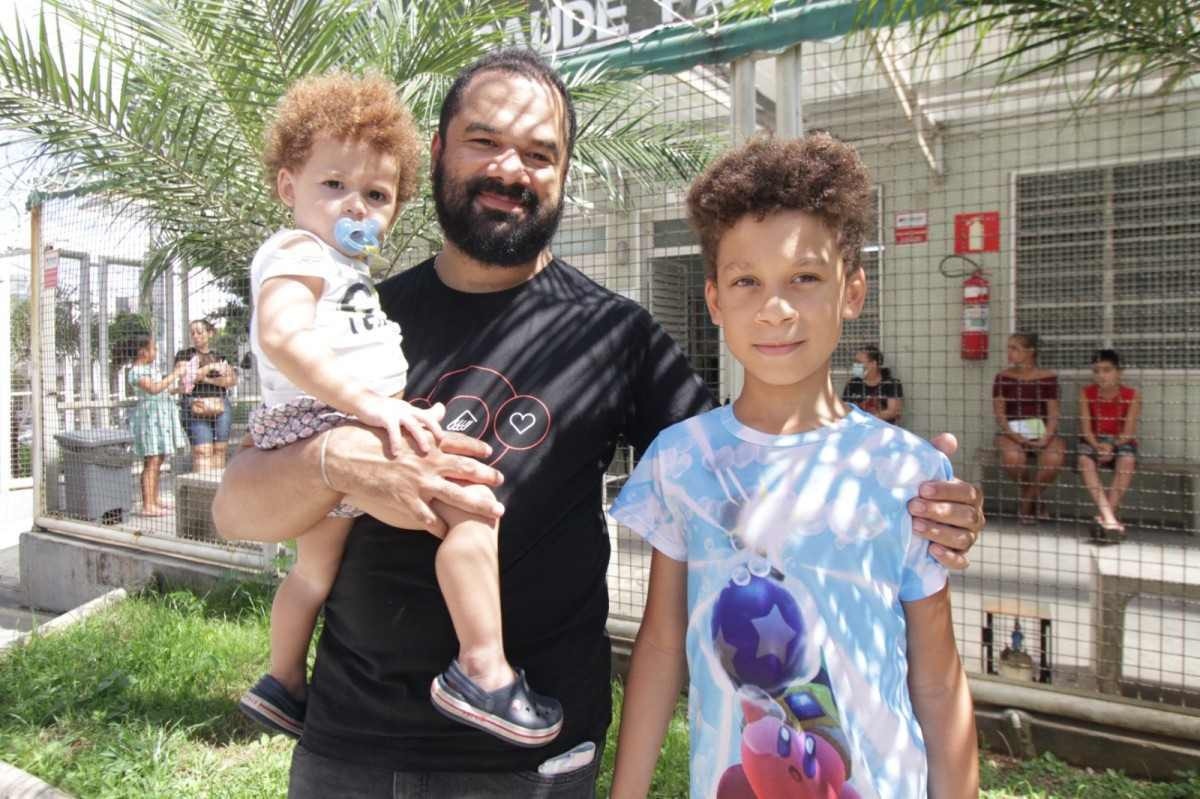 pai com filho no colo e abraçando outro que está ao lado dele