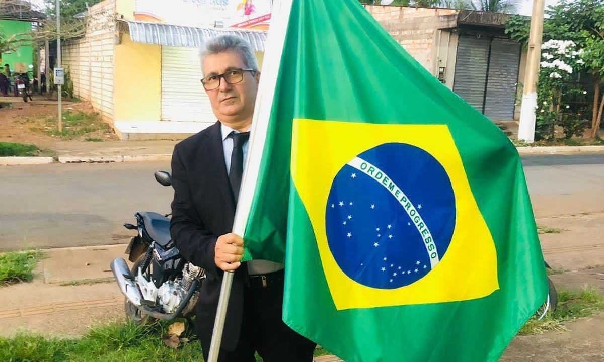 Darci Alves Pereira, de terno e gravata, segura a bandeira do Brasil -  (crédito: Facebook)