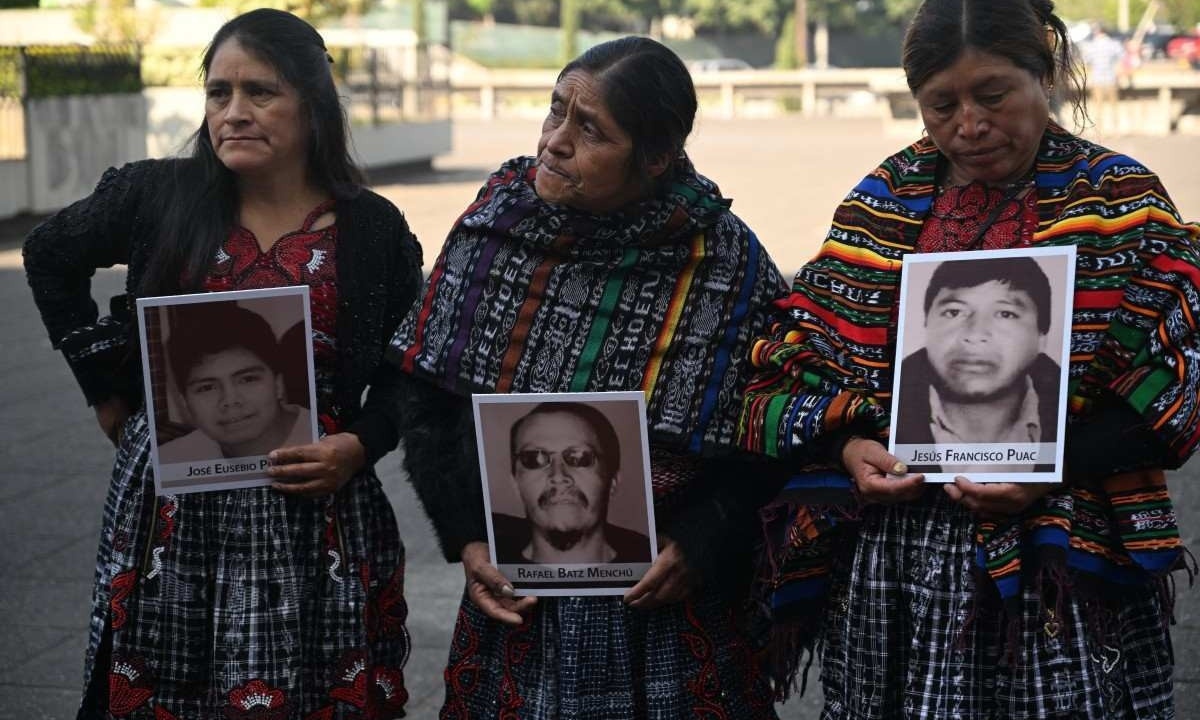 Parentes seguram retratos de três vítimas de um despejo rodoviário realizado pelos militares em 2012, durante uma cerimônia maia em frente ao Palácio da Justiça na Cidade da Guatemala       -  (crédito: JOHAN ORDONEZ / AFP)