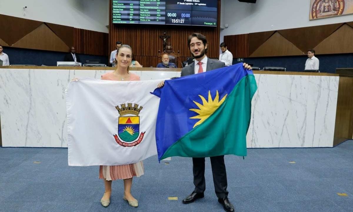 A vereadora Fernanda Pereira Altoé (Novo) segura a bandeira atual de Belo Horizonte ao lado do presidente da Casa, Gabriel Azevedo (MDB), que exibe a proposta do novo modelo -  (crédito: Câmara Municipal de BH)