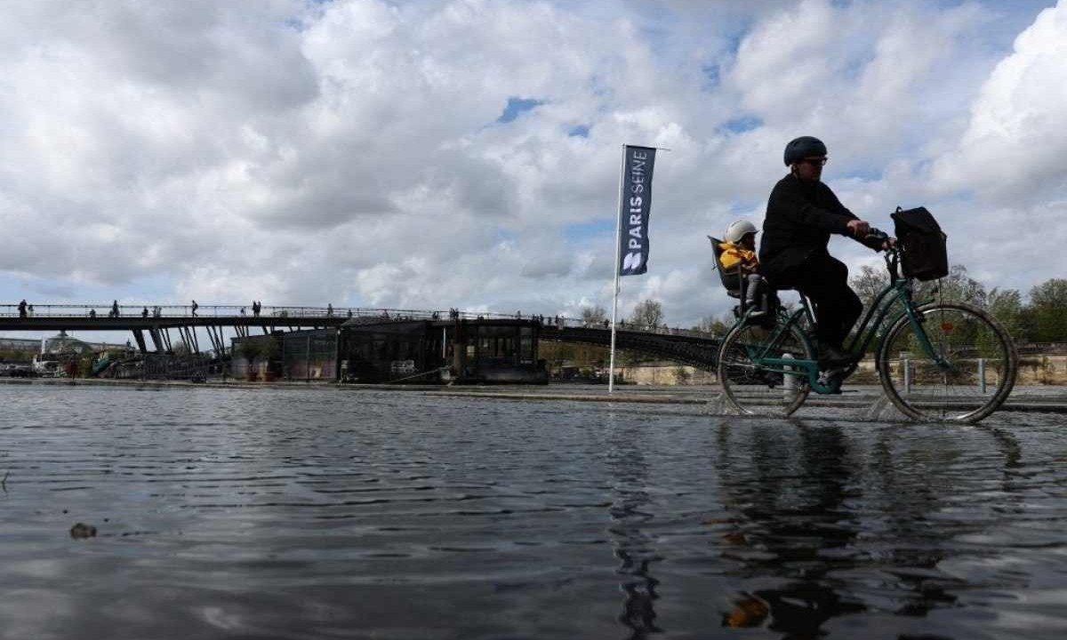  Homem carrega uma criança de bicicleta pelas docas inundadas ao longo do rio Sena, em Paris -  (crédito: Emmanuel Dunand / AFP)