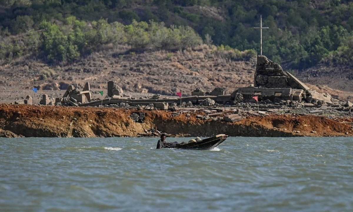 Homem passa de barco pelas ruínas de igreja na antiga cidade submersa de Pantabanga, cujos restos ressurgiram quando o nível da água de uma barragem caiu por causa da seca nas Filipinas
       -  (crédito: JAM STA ROSA / AFP)