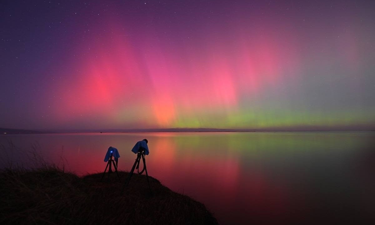 A configuração da câmera de um fotógrafo é vista enquanto a Aurora Australis, também conhecida como Luzes do Sul, brilha no horizonte sobre as águas do Lago Ellesmere, nos arredores de Christchurch, em 11 de maio de 2024 -  (crédito: Sanka Vidanagama/AFP)