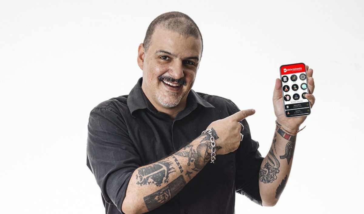 Homem com tatuagens segurando um celular acessando um APP para tira dúvidas