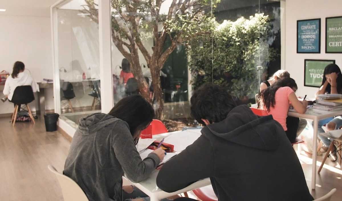 Alunos estudando dentro de uma sala de estudos de vidro com um pé de jabuticaba no meio da sala
