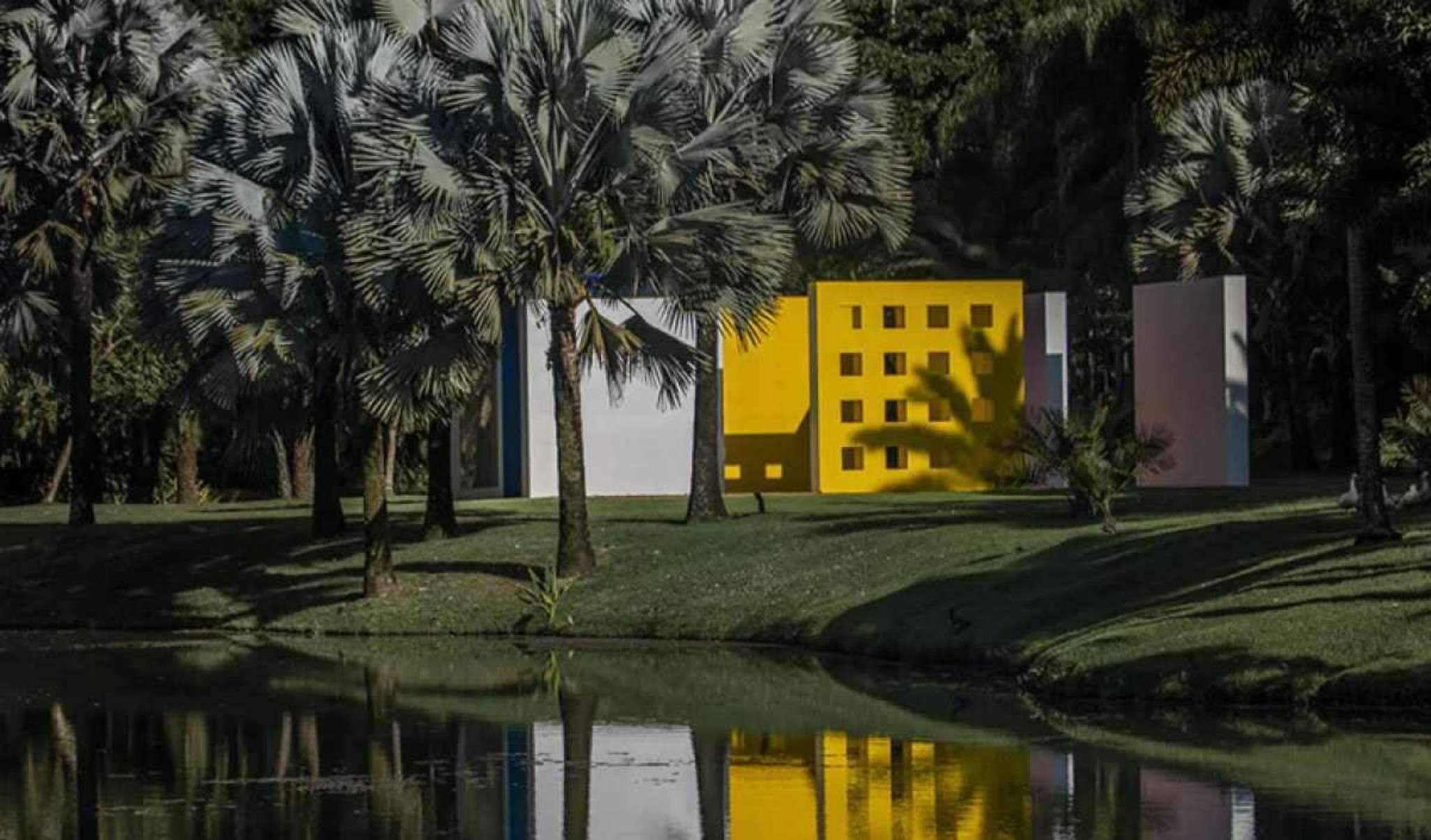 Casa amarela ao lado de árvores e uma lagoa