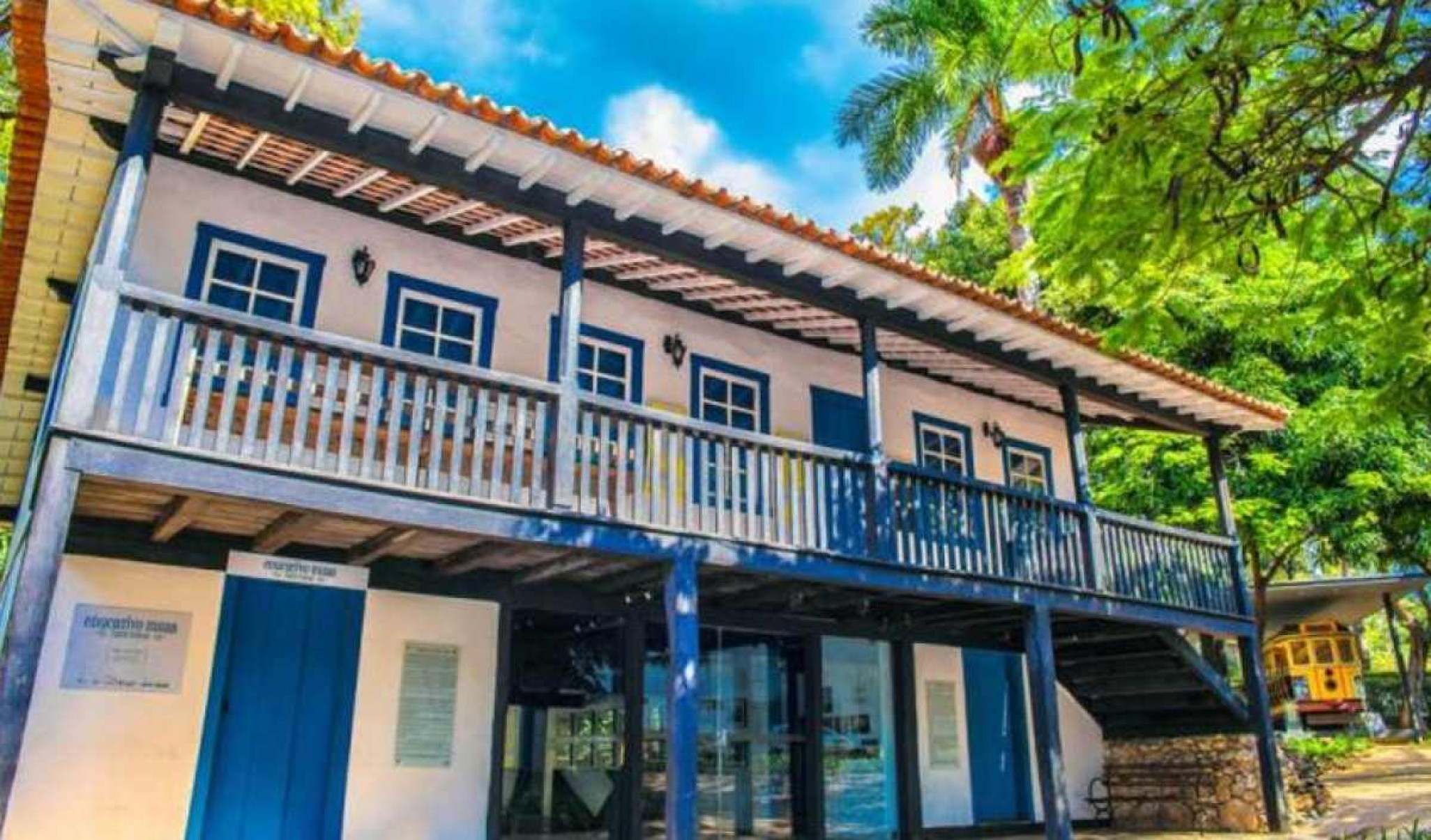 Casa história com varanda e janelas azuis ao lado de uma árvores