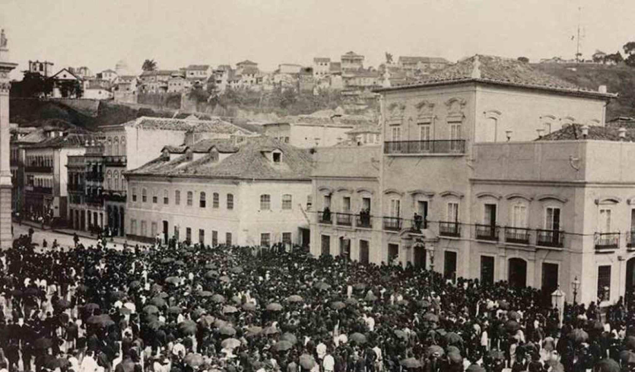 Imagem histórica mostrando uma multidão de pessoas na frente de uma edificação de 1800.