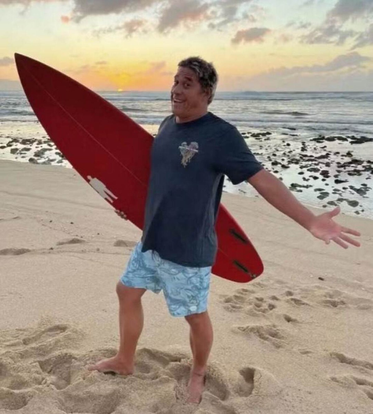 Tamayo Perry sorrindo com a prancha de surfe, esporte que adorava praticar