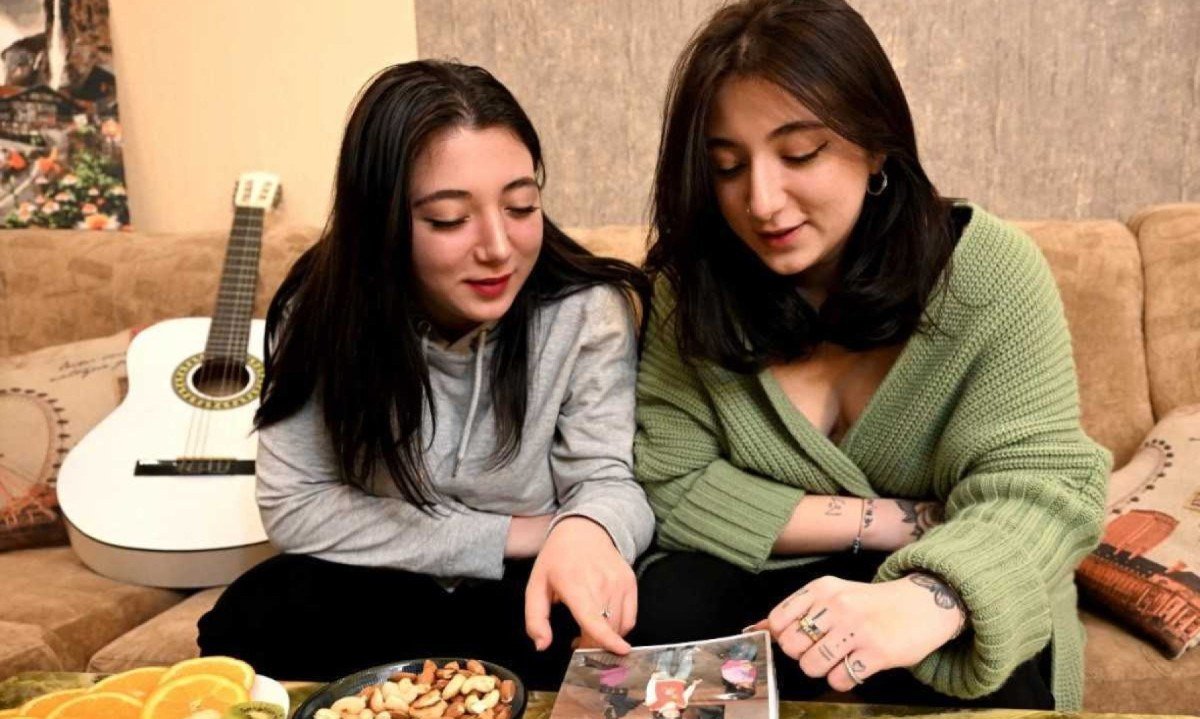 Irmãs gêmeas georgianas Anna Panchulidze (E) e Elene Deisadze olham fotos em álbum  -  (crédito: Vano SHLAMOV / AFP)