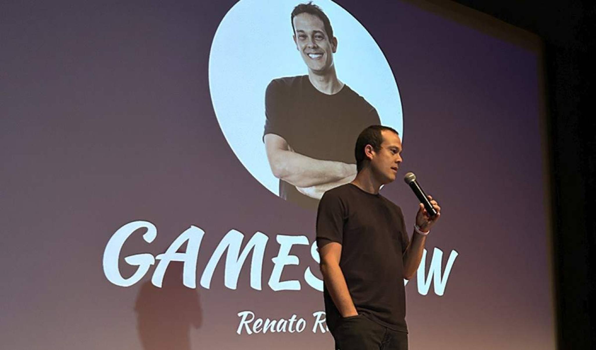 Homem de meia idade no palco de um teatro apresentando uma aula.