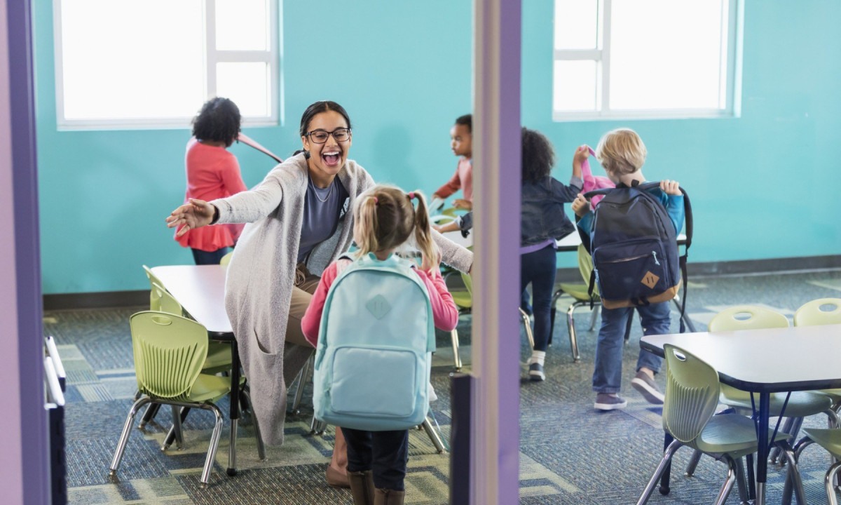  A mixed race African-American and Caucasian woman, a preschool teacher sitting in her classroom, greets one of her students, a little girl, 4 years old, walking through the doorway. Other students have already entered and are sitting down behind her.
       -  (crédito:  Getty Images)