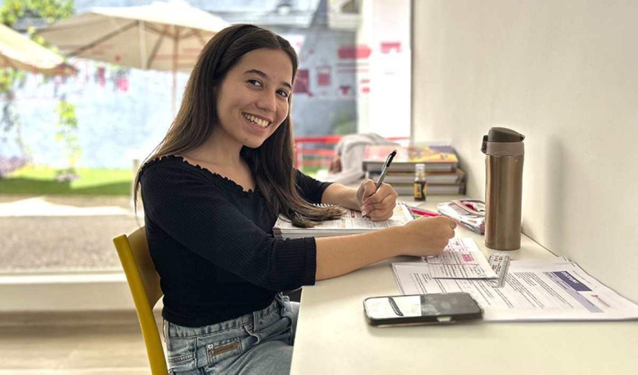 Jovem aluna estudando em uma sala de vidro.