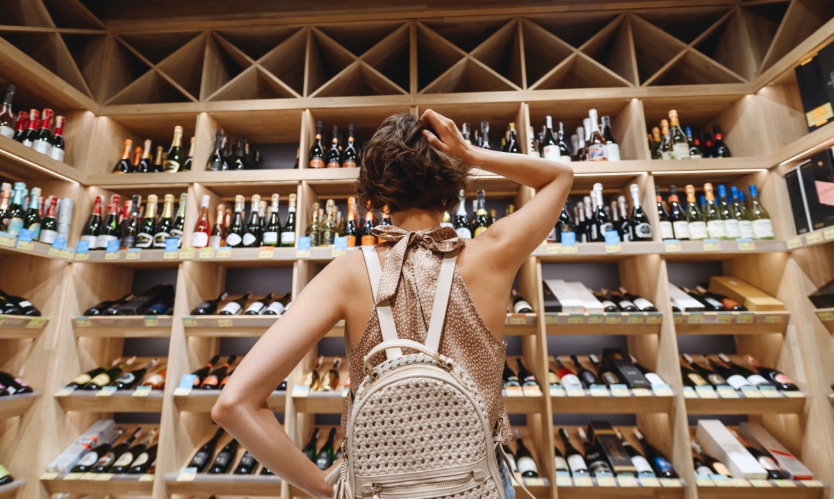  Back view puzzled young woman 20s wear casual clothes shopping at supermaket grocery store buy choosing wine alcohol bottle scratch head inside hypermarket. People purchasing gastronomy food concept
     -  (crédito:  Getty Images)