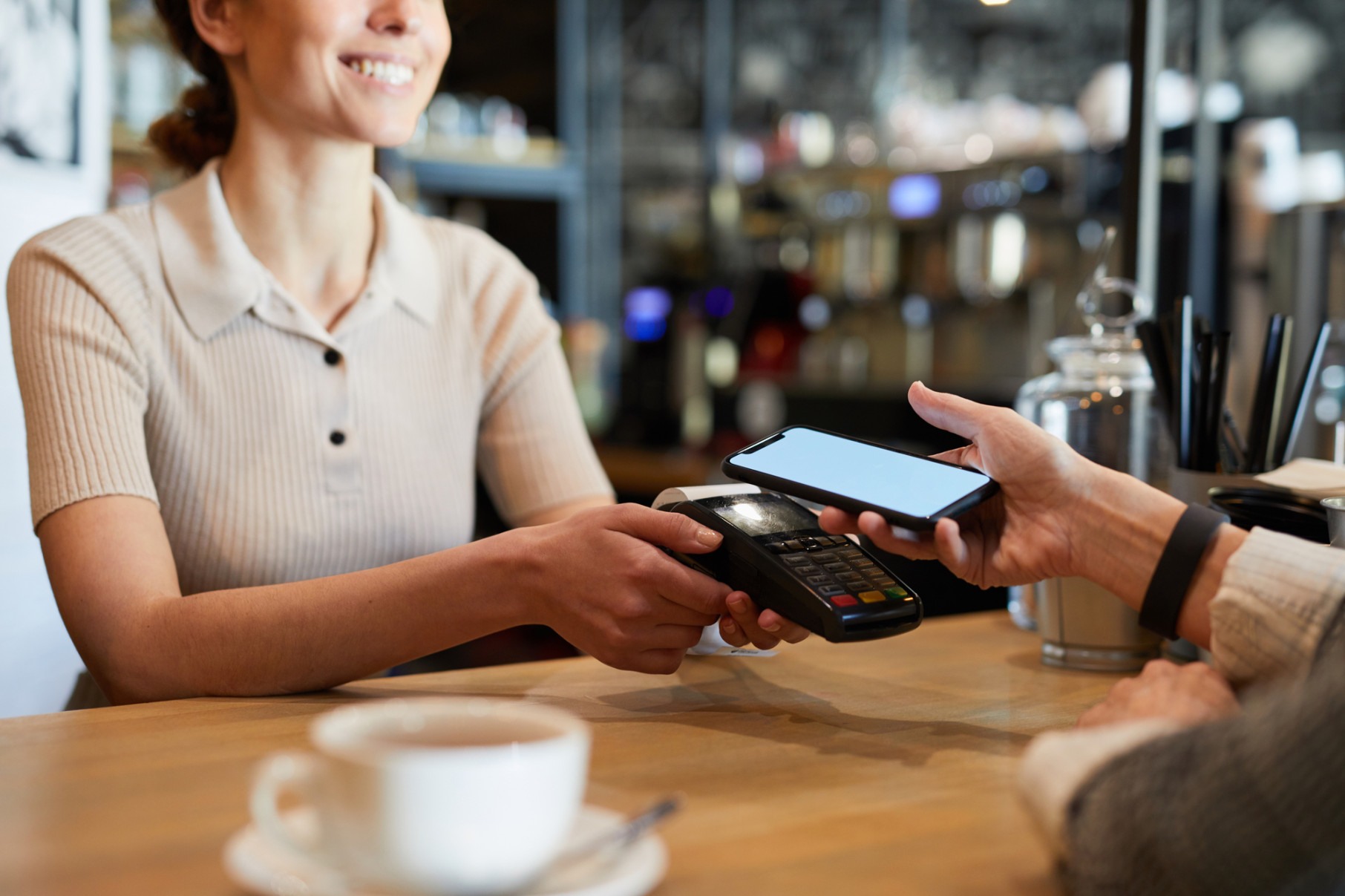  Young waitress standing by bar counter while holding electronic payment machine and waiting for client with smartphone paying for drink
     -  (crédito: DINO)