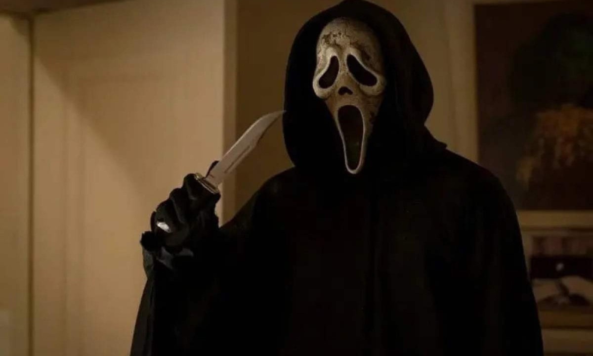 Ghostface, personagem que veste manto preto e máscara branca. Ele ainda segura uma faca na mão direita.