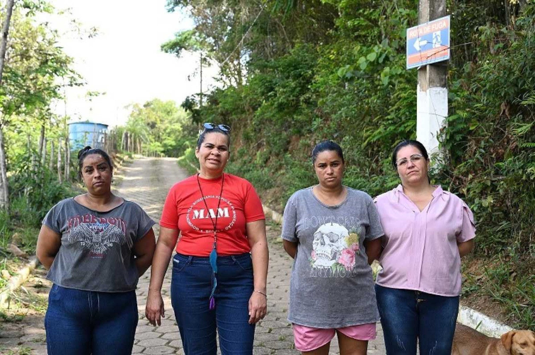 Daniela, Roseni, Silvana e Ana paula diante da placa que consideram errada em rota de fuga, por estar voltada para a barragem. Mineradora afirma que posicionamento é correto