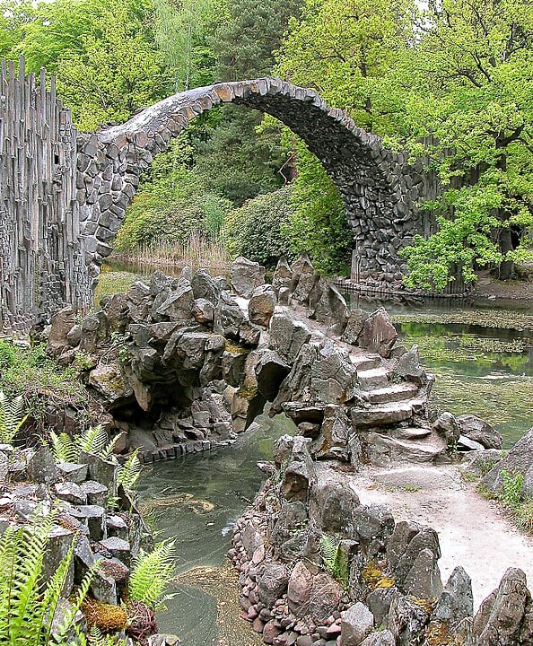 A ponte é feita de pedras e basalto, dispostas de maneira a criar um visual rústico e ao mesmo tempo encantador, dando a sensação de que a estrutura faz parte da paisagem natural ao redor.