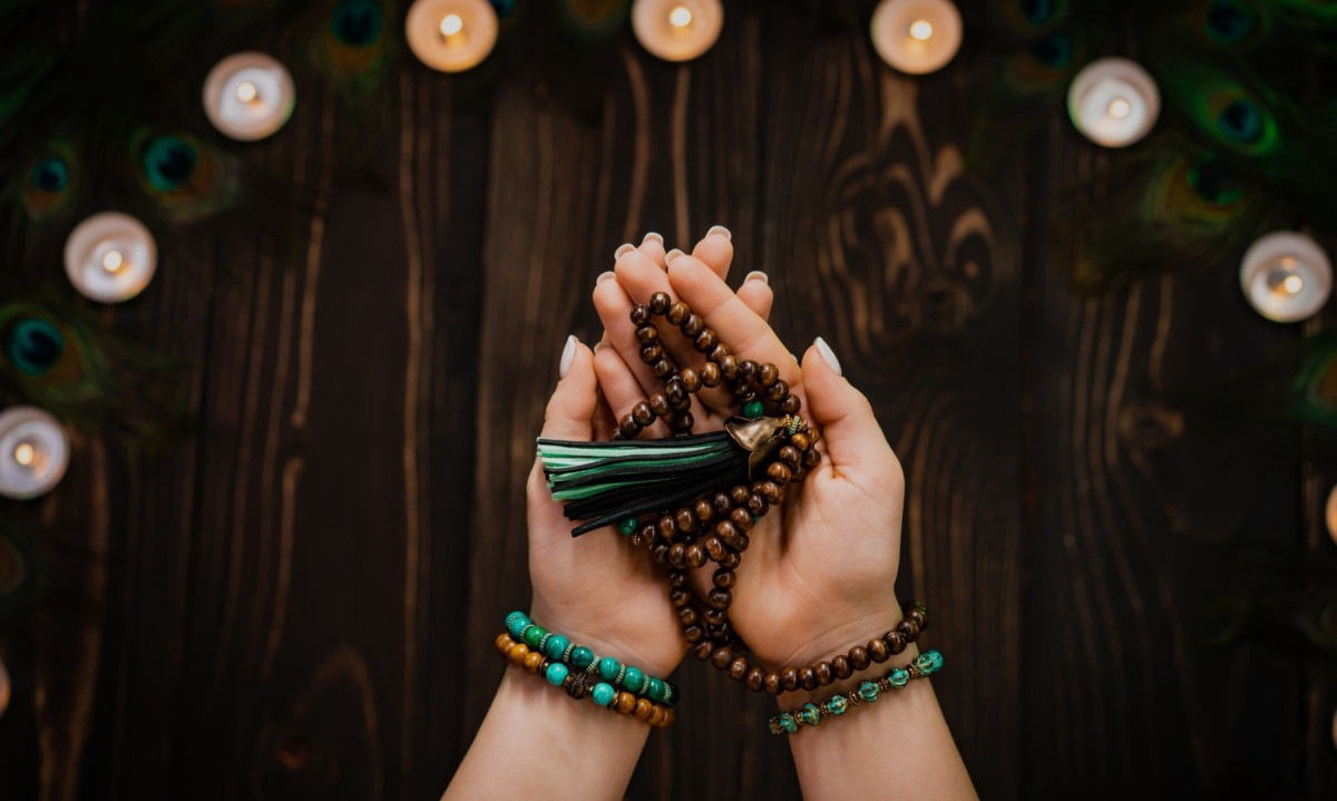  Woman holds in hand wooden mala beads strands used for keeping count during mantra meditations. Weaving and creation. Wooden background with candles and feathers. Spirituality, religion, God concept -  (crédito: Wemystic)