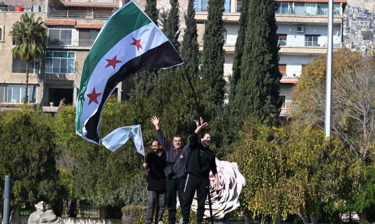 Homens sírios agitam a bandeira da oposição enquanto estão onde a estátua de um soldado sírio foi derrubada pelos rebeldes na praça central Umayyad, em Damasco, em 9 de dezembro de 2024  


 -  (crédito:  LOUAI BESHARA / AFP)