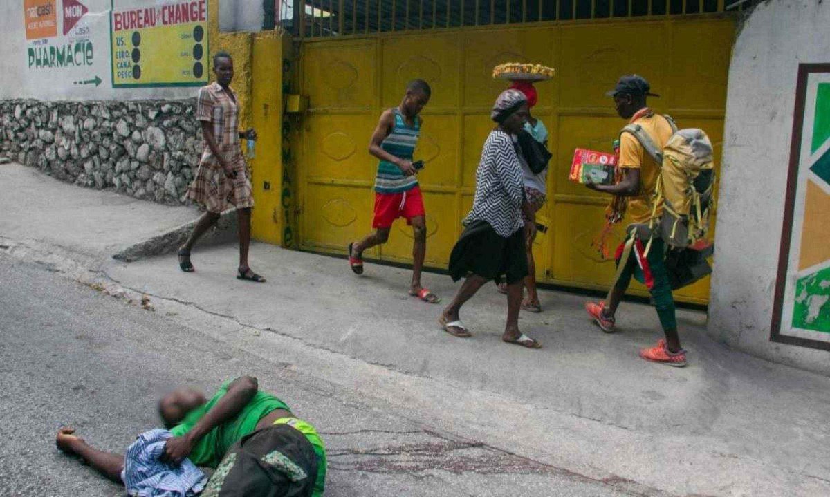 Pessoas passam pelo corpo de um homem morto a tiros por homens armados; confronto de gangues no Haiti têm sido comuns nos últimos anos -  (crédito: Clarens SIFFROY / AFP)