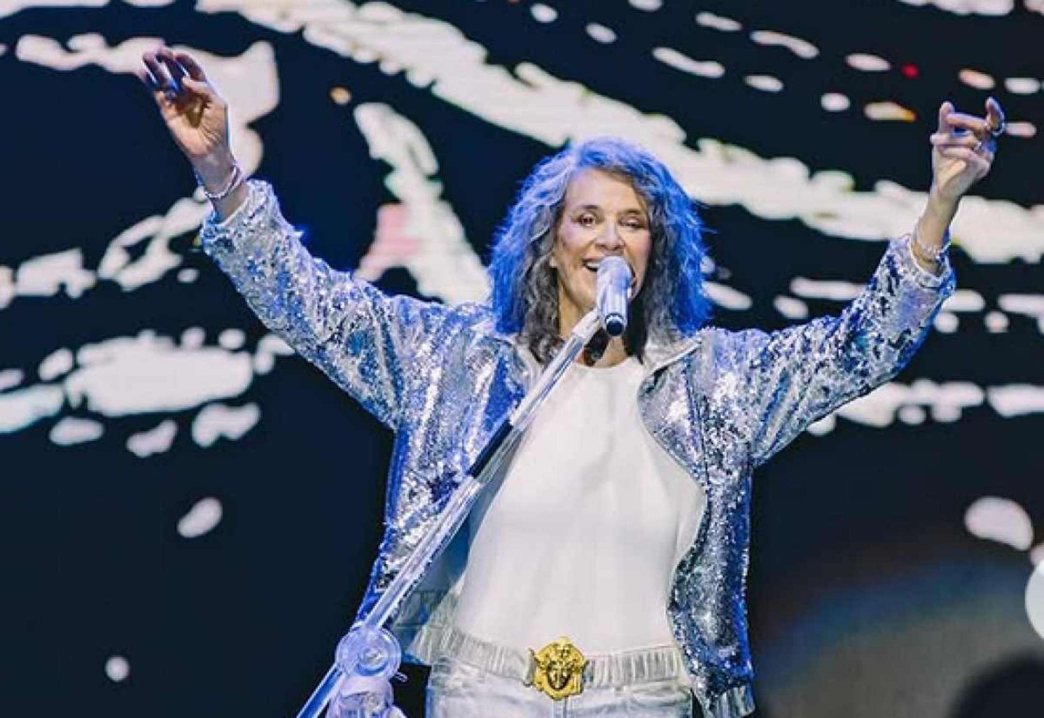 Cantora Simone usa blusa azul e abre os braços ao cantar no palco. Ela é dona do hit Então é natal