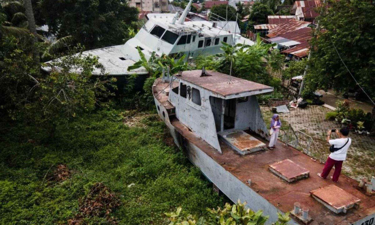 Pessoas tiram fotos em um dos dois barcos patrulha levados à costa pelo tsunami do Oceano Índico de 2004 e preservados na comunidade em Banda Aceh
       -  (crédito: Yasuyoshi CHIBA / AFP)