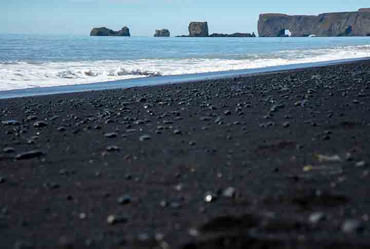 Praia de Reynisfjara – Vík í Mýrdal, Islândia - Famosa por sua areia negra vulcânica, contraste impressionante com os pilares de basalto e o Atlântico. É cercada por uma paisagem dramática e surreal.
