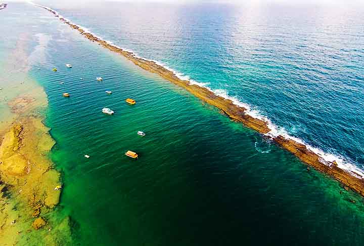 Praia do Francês – Marechal Deodoro, Alagoas - Parte da areia apresenta tons amarelados e é cercada por trechos de recifes que criam um visual diferenciado. As águas variam entre azul e verde, refletindo na areia úmida.