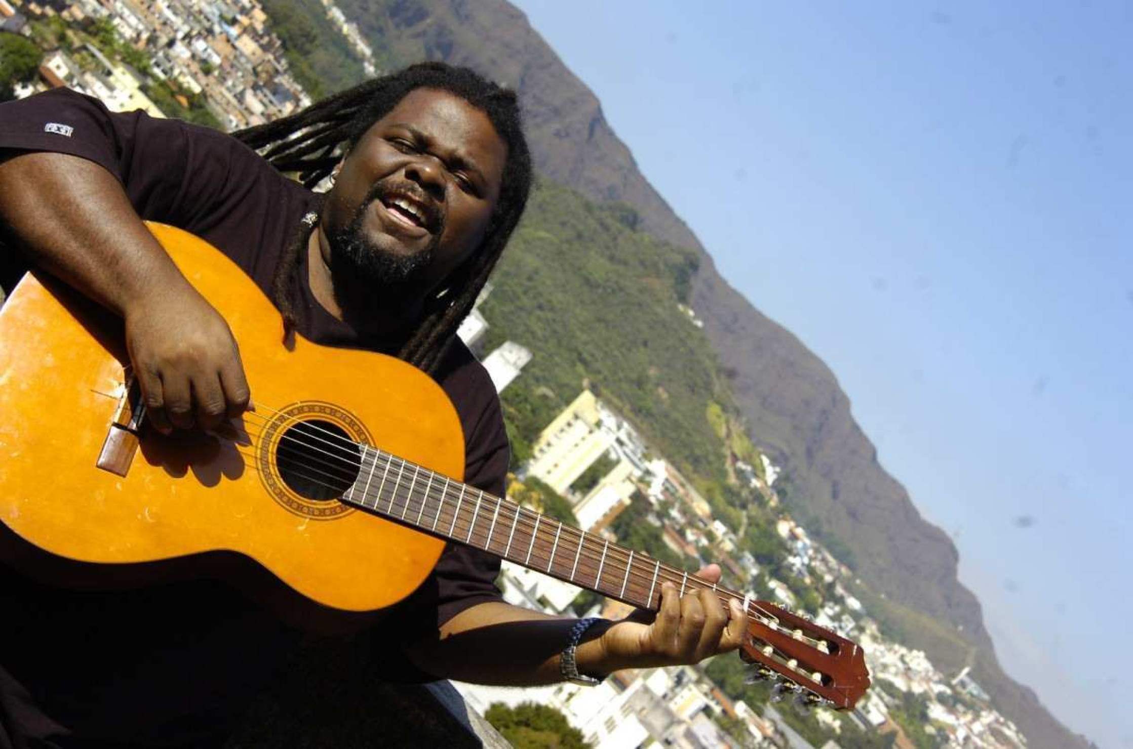 Mestre Jonas toca violão, tendo ao fundo a Serra do Curral e a paisagem de Belo Horizonte