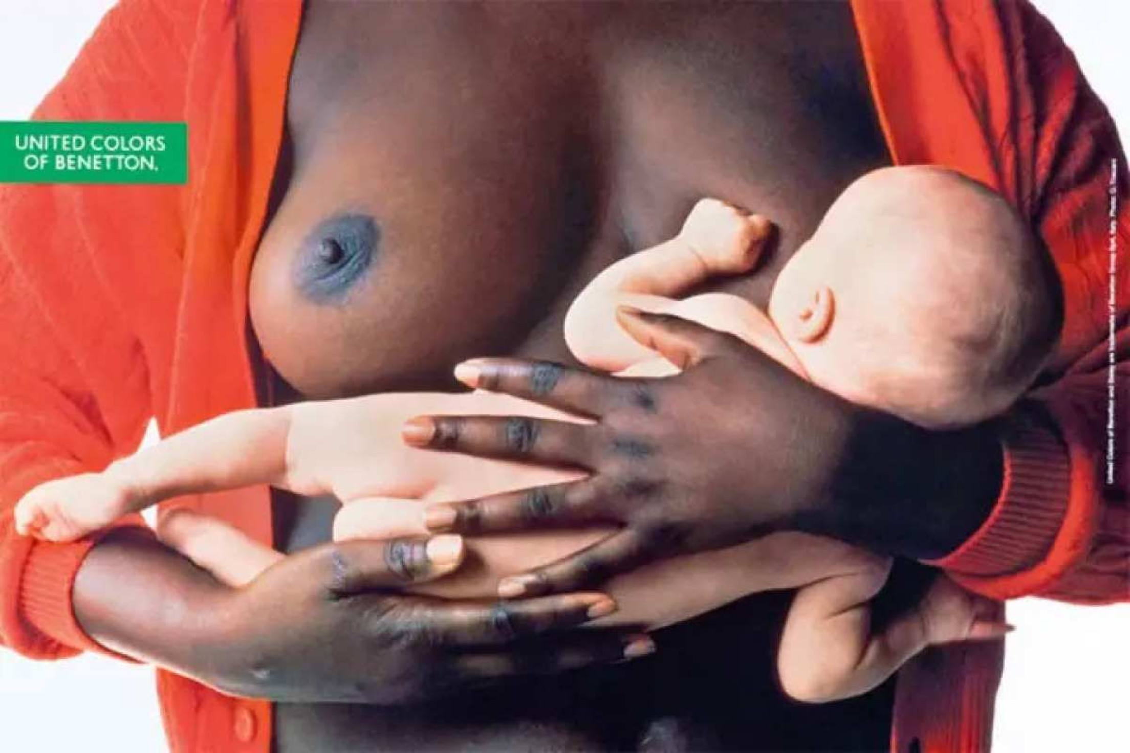 Mulher negra, vestindo casaco vermelho, amamenta criança branca em campanha publicitária criada por Oliviero Toscani para a grife Benetton