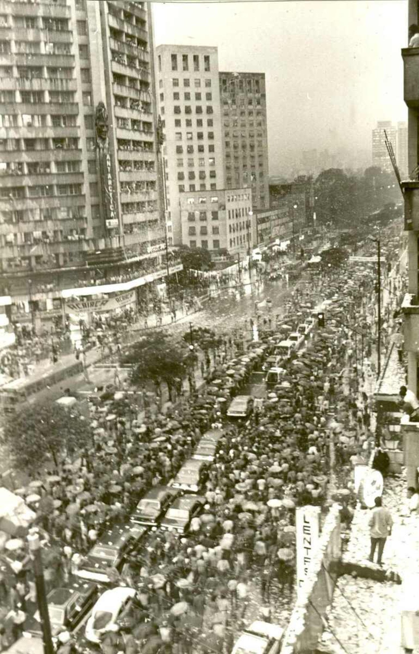O presidente eleito, Tancredo Neves, foi ovacionado debaixo de forte chuva, por dezenas de populares que o aguardavam ao longo da avenida Afonso Pena, quando de sua primeira visita a Minas Gerais depois de eleito
