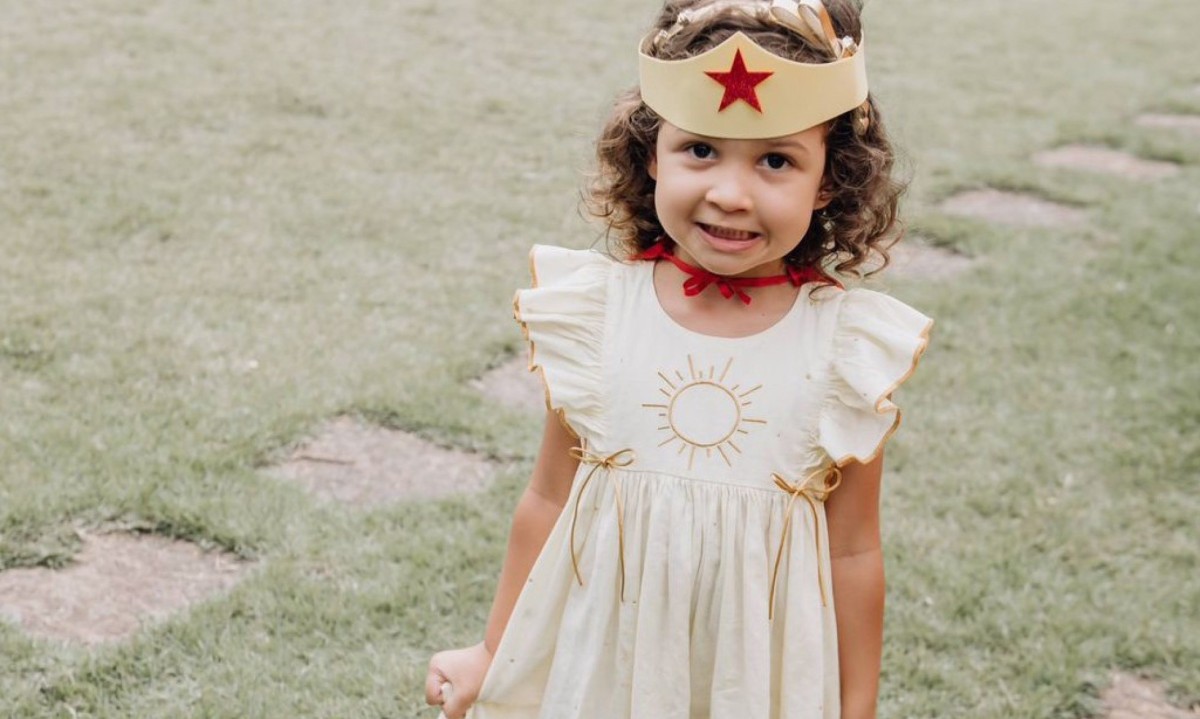 Julia Domingues, de 4 anos, que tem rara doença generativa, usa vestido branco e tem na cabeça a tiara da Mulher Maravilha 