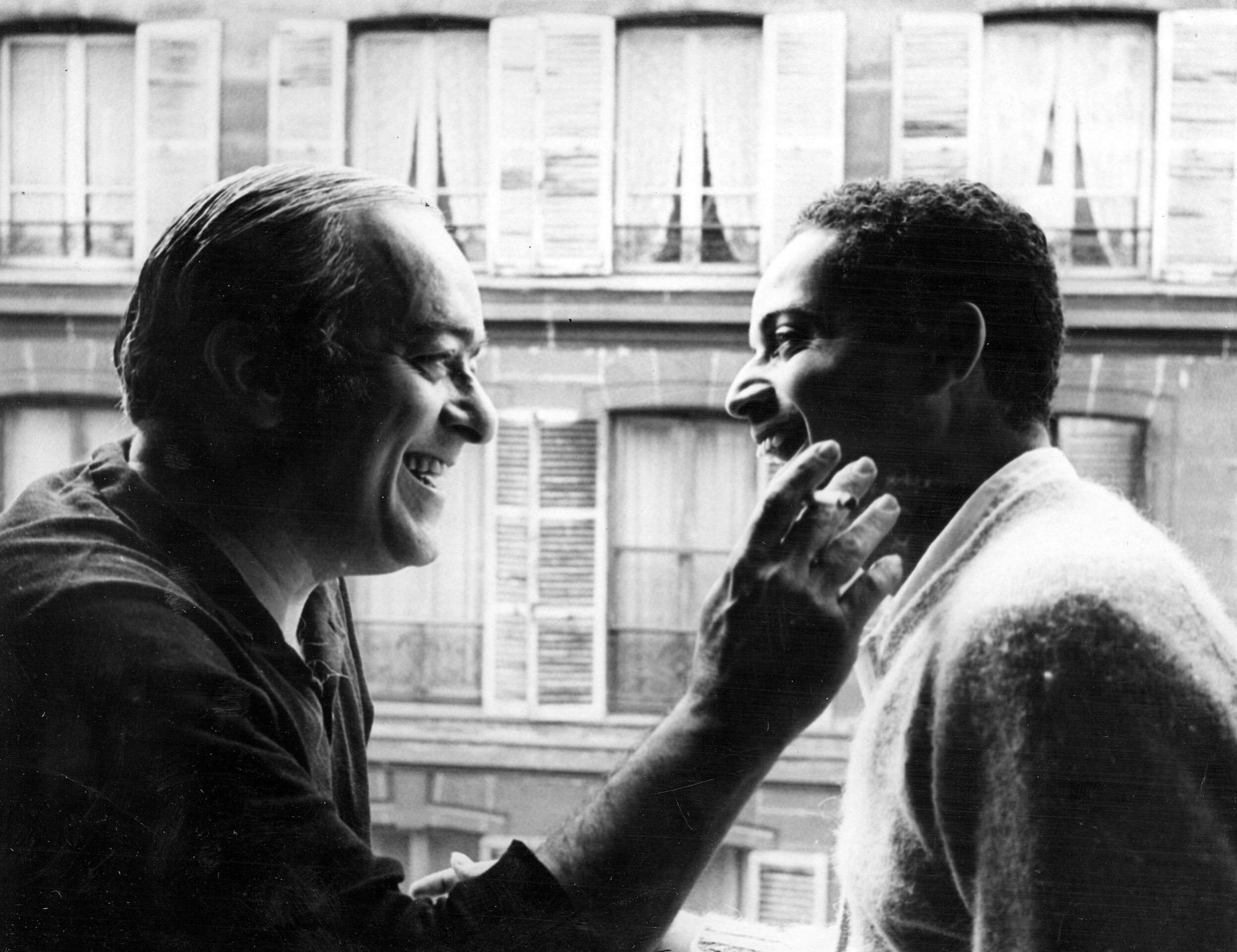 Vinicius de Moraes e Baden Powell estão de perfil, Vinicius toca o rosto de Baden com a mão direita